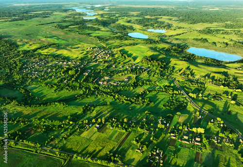 Fototapeta Naklejka Na Ścianę i Meble -  Village at lake, aerial view. Country houses at river in countryside. Roofs of country wooden houses near a pond in village. Green farm fields and forests in rural landscape. Farmland, Agriculture.