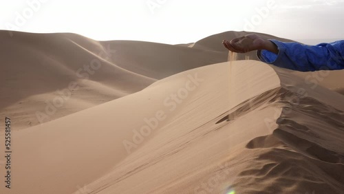 A Moroccan man, wearing a blue gandoura, djellaba and turban, rests on top of a sand dune playing with sand, Chigaga desert, Morocco. Authentic Bedouin of South Morocco. 4k footage. photo