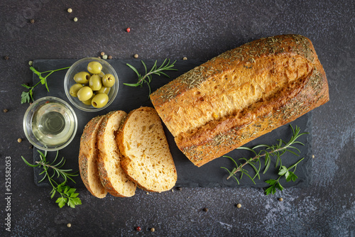 Fresh baked sliced Ciabatta bread with olives, oil bowl, herbs and spices closeup on stone board