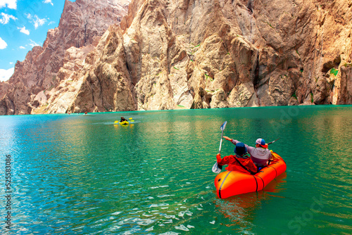 Kayaking on a mountain lake. Two men are sailing on a red canoe along the lake along the rocks. The theme of water sports and summer holidays.