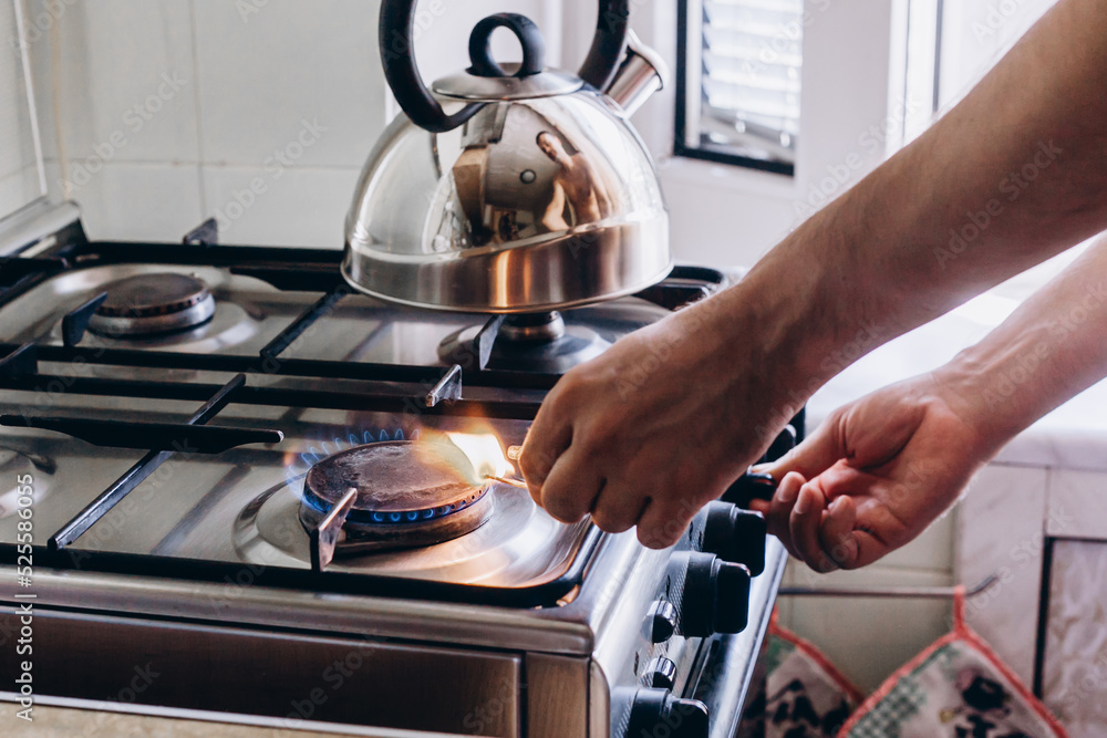 A man's hand with a match lights a gas burner or a gas stove in the kitchen
