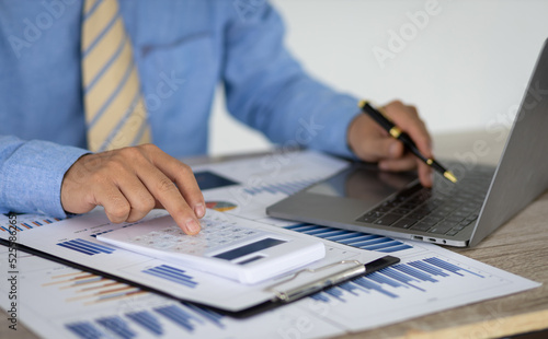 Businessman pointing at chart in document analyzing company sales and financial reports using laptop and budgeting power calculator. Financial planning and accounting.