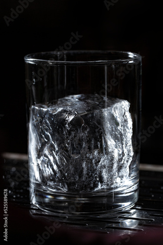 Crystal Clear Ice Cube sitting in Whiskey Rocks Glass on Bar Top