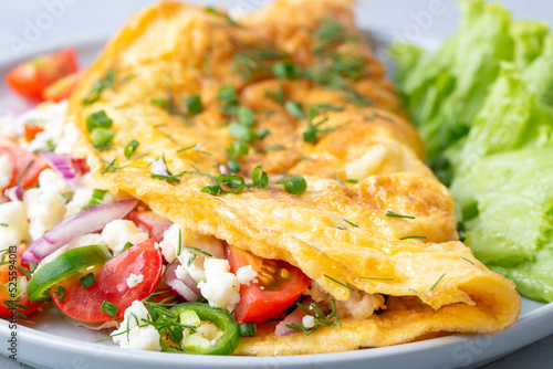 Homemade stuffed omelet on a plate. Egg omelet stuffed with fresh tomatoes, cheese and green parsley. Healthy vegetarian breakfast recipe.