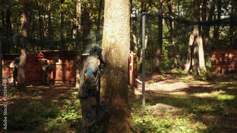 Men wears camouflage and protective mask while participating in a paintball battle game with friends, takes part in leisure activities. Men wears camouflage and protective mask while participating in a paintball battle game with friends, takes part in leisure activities.