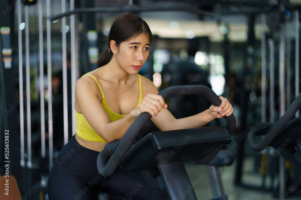 Beautiful Asian woman is working out in the gym by bike to get strong and beautiful muscled. Beautiful Asian woman is working out in the gym by bike to get strong and beautiful muscled.