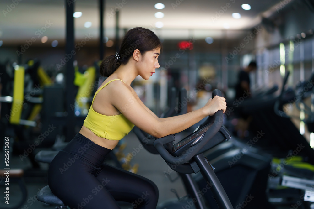 Beautiful Asian woman is working out in the gym by bike to get strong and beautiful muscled. Beautiful Asian woman is working out in the gym by bike to get strong and beautiful muscled.