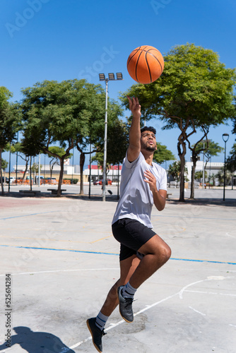 Vertical portrait of a young muslim man playing street basketball, jumping, on a city court, training and sport concept