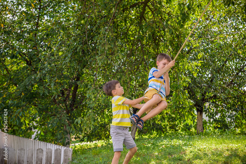 Two adorable happy little boys is having fun on a rope swing which he has found while having rest outside city. Active leisure time with children