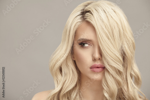 Blonde woman with long wavy hair looks aside on beige isolated background with free copy space.