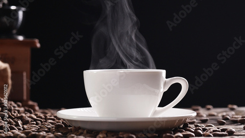 Hot Coffee Cup Concept. Close-up white coffee cup, mug with beautiful steaming smoke, classic vintage coffee grinder espresso manual, beans, burlap on on old wooden table dark, black background. Hot D