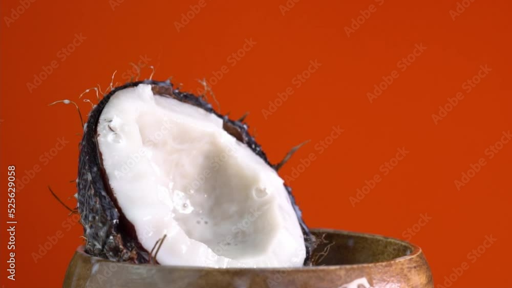Cracked fresh coconut with splashing milk. Drops of coconuts oil over red background, dripping