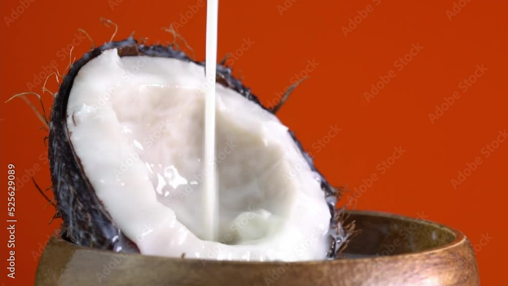Dripping coconut water, drops of coconuts oil over red background, coconut milk pouring. Cracked