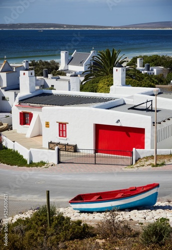 Vertical of white buildings with red doors and window shutters by the Atlantic Ocean in Western Cape