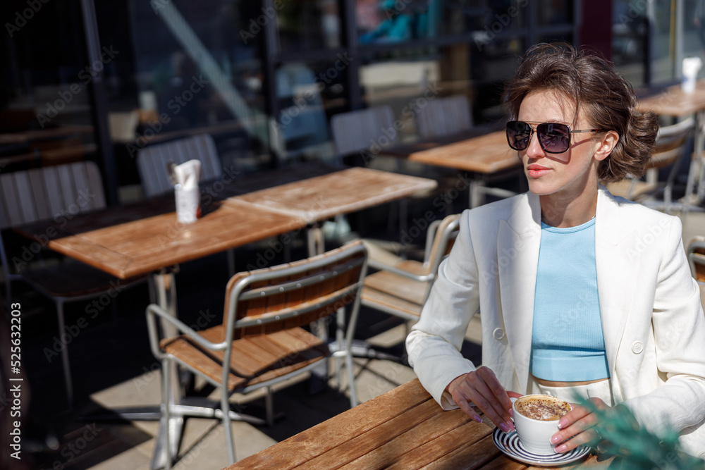 Attractive business woman in sunglasses drinking coffee sitting in cafe