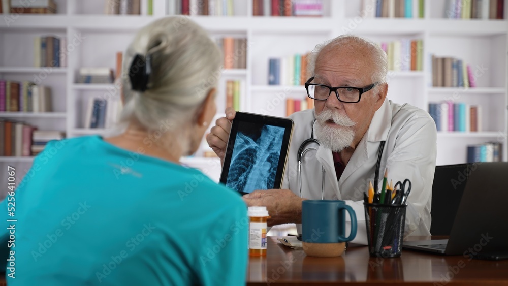 Elderly male doctor consults with woman patient looking at tablet computer showing x-ray.
