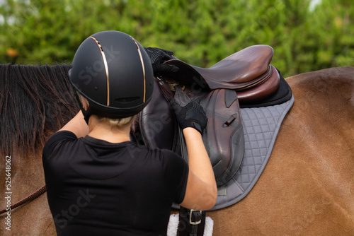 Woman adjusting stirrup on English saddle. 