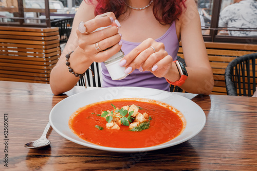 A woman adds salt from a saltcellar to soup in a restaurant. An overabundance of consumption of this seasoning can lead to cardiovascular diseases and gout