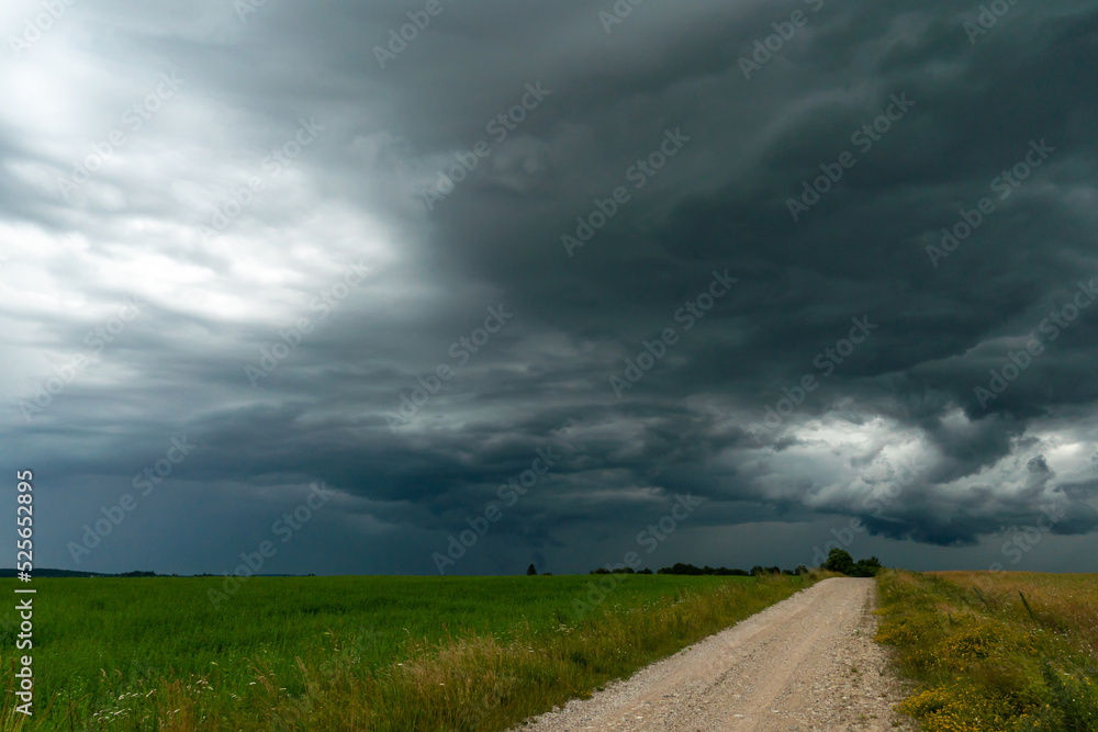 A rainy gray cloud hovered over the field. A hurricane over an agricultural field. Dirt country road, dramatic scene. A rainy gray cloud hovered over the field. A hurricane over an agricultural field. Dirt country road, dramatic scene.
