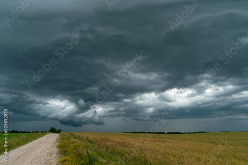A rainy gray cloud hovered over the field. A hurricane over an agricultural field. Dirt country road, dramatic scene.