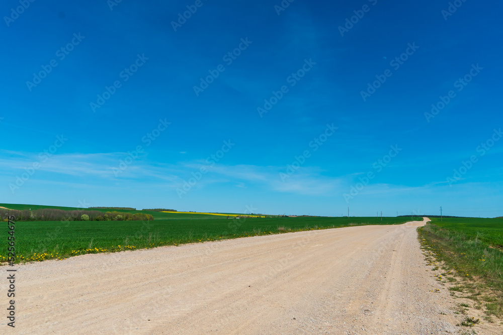 A dry sandy road passes through a field under the scorching sun and clouds. Dirt road outside the city in the village. Arid climate on earth. Climate change and its consequences.