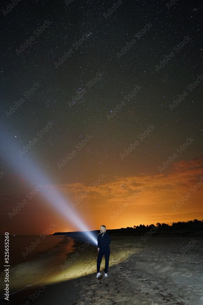 Starry sky and girl on the beach with flashlight 