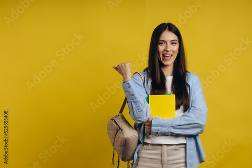 Successful young college student holding books and shaking hands on yellow background. The concept of learning in school and college
