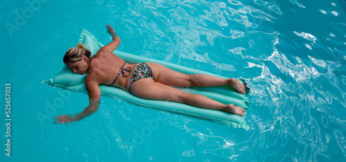 Femme blonde allongée sur le ventre en train de bronzer sur un matelas pneumatique dans une piscine bleue