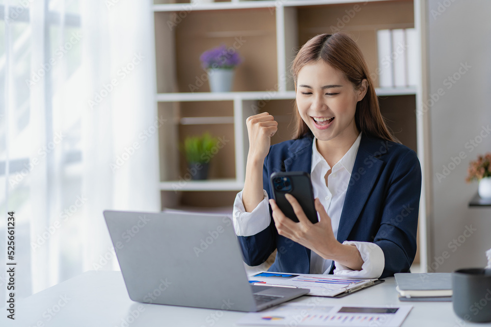Successful young Asian businesswoman uses smartphone and laptop to work in office with financial graph document on desk. Successful young Asian businesswoman uses smartphone and laptop to work in office with financial graph document on desk.