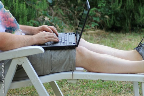 Caucasian man working on a laptop in the garden sitting on a deck chair. photo