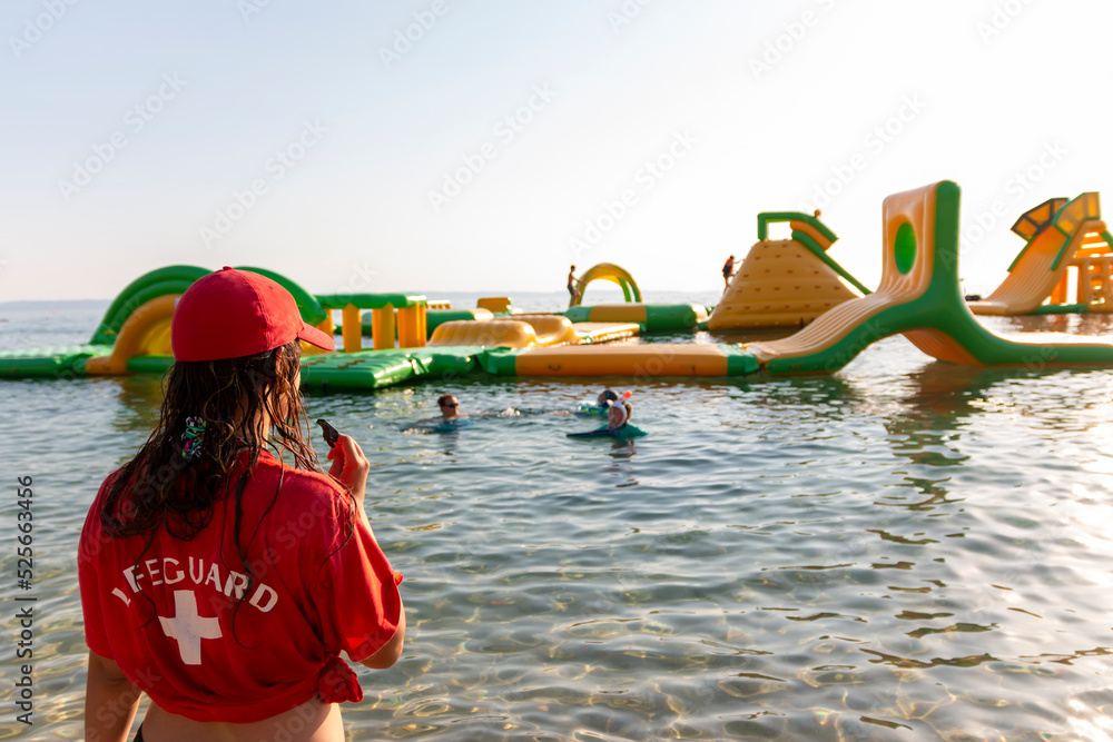 Lifeguard on rescue duty, standing on shore with whistle and looking to the Aquapark. Safety control on vacation. Babysitting on the water