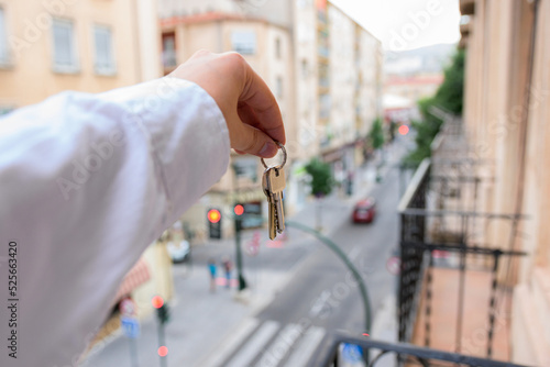 A man holds keys in a house with buildings in the background. Real state concept