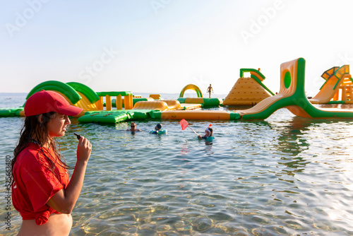 Lifeguard on rescue duty, standing on shore with whistle and looking to the Aquapark. Safety control on vacation. Babysitting on the water photo