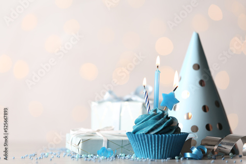 Delicious birthday cupcake with cream and burning candles on white table. Space for text