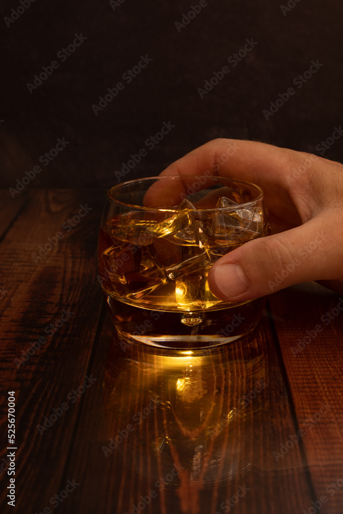  liquor glasses of whiskey, rum, etc., lit liquor from inside the glass with ice cubes one hand holds the glass stone tray or plate slate wooden table vertical photo with space for text