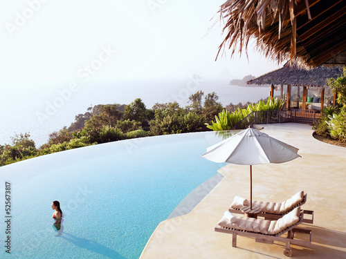 A woman stands in a luxury infinity pool overlooking  Phang Nga Bay, Yao Noi, Thailand.