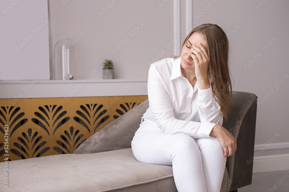 Cute girl with her eyes closed covers her face with her hand while sitting on the couch Cute girl with her eyes closed covers her face with her hand while sitting on the couch