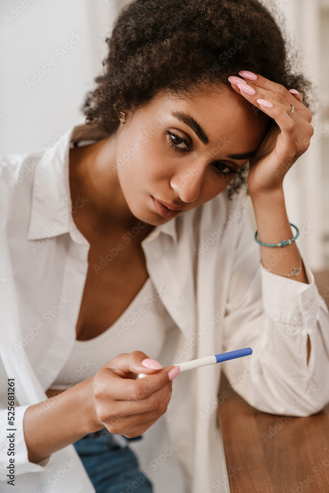 Young black woman being upset while holding pregnancy test at home Young black woman being upset while holding pregnancy test at home