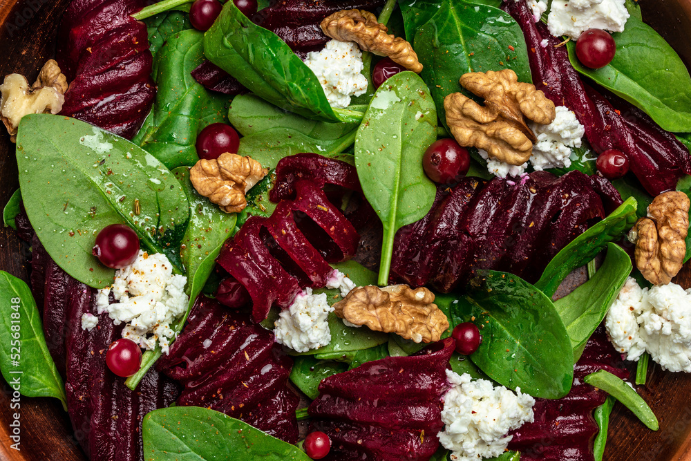 Close up Beet or beetroot salad with baby spinach, cheese, nuts, cranberries on plate, dressing and spices. top view