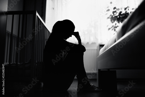 Silhouette of tired, stressed mother sitting next to baby crib at home.