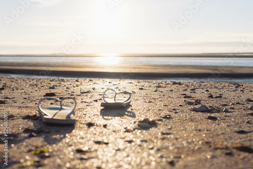 on beach on the sand a pair of beach slippers stands close-up and the background is blurred at sunset, the photo is taken, a beautiful and creative beach background with a place for an inscription