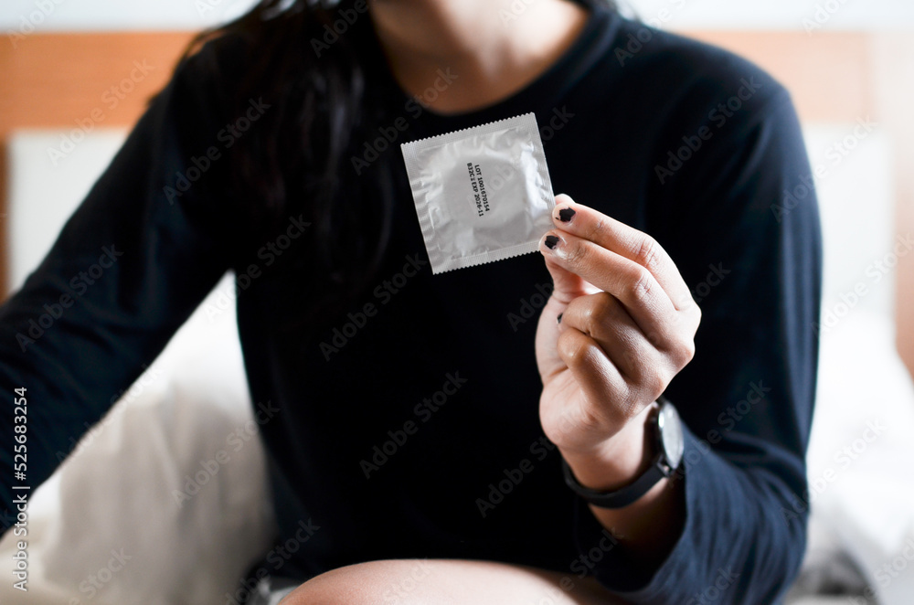 Unrecognizable woman hands holding condom on a bed. focus at hand. safe sex concept. Unrecognizable woman hands holding condom on a bed. focus at hand. safe sex concept.