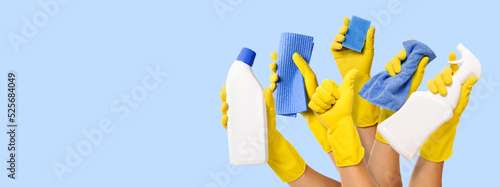 hand with yellow rubber glove holding cleaning supplies on blue background. banner with copy space photo