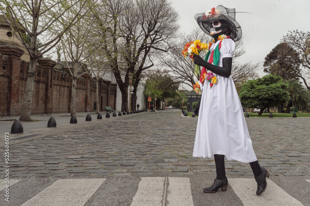 An adult woman with face painted and costume as Calavera Catrina walking on a crosswalk.