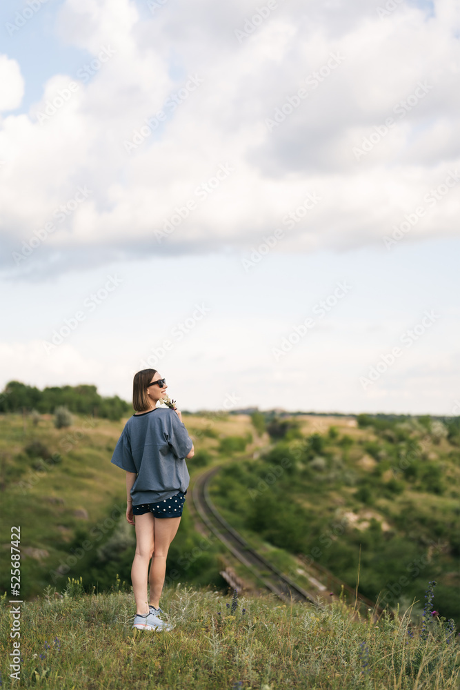 Carefree young woman daydreaming in nature with beautiful clouds in background