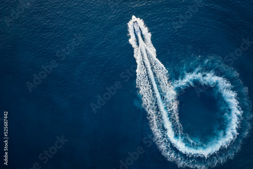 Aerial top view of a motor powerboat forming a circle of waves and bubbles with its engines over the blue sea photo