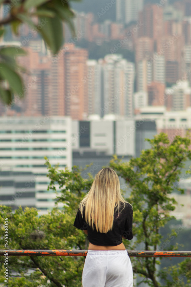 Blonde woman from behind at a viewpoint observing a city out of focus in the background Blonde woman from behind at a viewpoint observing a city out of focus in the background