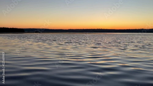 Calm river, slight waves, reflection and glare right before sunrise. Clear golden orange sky, first rays of rising sun. Early morning over the lake. 4k
