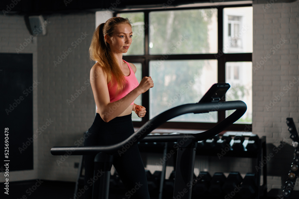 Athletic build girl doing cardio training exercise by jogging on a treadmill in the gym