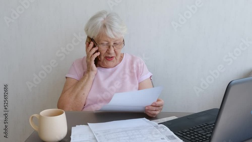 Senior woman holding papers busy at laptop managing house utility bills or finances, aged female using computer working with bank loan or mortgage documents online. Elderly and technology concept. tal